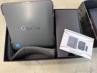 GUZILA Mini PC in black with Intel sticker on front side, inside original box alongside user manuals and quick start guide.