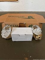 Pair of clear glass or crystal-effect branded Nostalgic Warehouse door knobs on brass bases in original packaging.