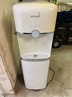 Front view of the white Primo water dispenser with dispensing area and control button visible.