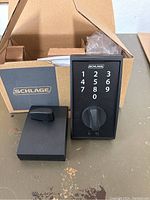 Photo of Schlage touchscreen deadbolt lock with keypad and thumb turn, showing unit outside of the box along with instruction manual.