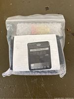Photo of the Sky Quality Meter sealed in a plastic zip bag with printed manual showing the device and its digital display.