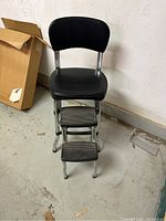 Front view showing black padded seat and backrest with two metal step footrests.