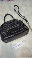 Black Danier purse with quilted design, front zipper pocket with tassel pull, double handles, and chain/leather strap, bottom metal feet visible.