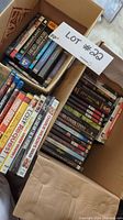 Photo of DVDs and Blu-Rays in a cardboard box showing multiple titles visible from above with a lot number card.