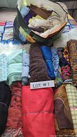 Top-down image showing assorted rolled and bundled fabrics in various colors and patterns arranged in a bag and outside with a visible lot number label.