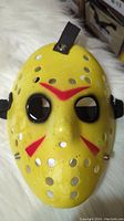 Front view of yellow Friday The 13th style hockey mask with red markings and ventilation holes