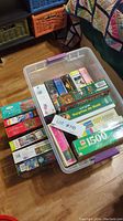 Large clear plastic storage bin contains multiple boxed jigsaw puzzles of varying themes and sizes placed inside and around it.