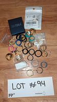 Photo displays assortment of rings in various materials and colors scattered on floor with lot identification card.
