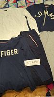 Photo showing four Tommy Hilfiger clothing items: white knit sweater, navy sweatshirt, navy zip-up hoodie, and navy sweatpants laid on colorful patchwork quilt.
