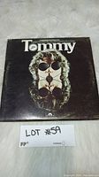 Front cover of vinyl album "Tommy" by The Who showing artistic design with face and sunglasses.