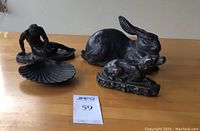Four cast iron sculptures including dying Gaul figure, rabbit, shell, Victorian dog doorstop reproduction on a wooden table.