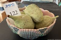 View of the ceramic bowl filled with the five faux gourds on a black surface showing scalloped edge and multicolored glaze