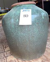 Full view of green glazed stoneware jar with auction lot number on front, showing textured surface.