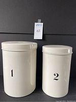 Front view of two off-white ceramic ironstone canisters with lids numbered 1 and 2.