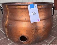 Side view of large copper pot showing patina, drain hole, and iron handle.