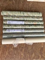 All seven wallpaper rolls laid side by side on wood floor, showing patterns and roll count