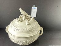 Full view of Mottahedeh soup tureen with lid and bird finial, cream color, raised floral design.