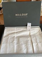 Open Malouf branded box showing folded white sheets inside.