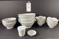 Photo showing entire lot of porcelain bowls and espresso cup on black surface against black background with auction label.