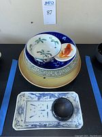 Stacked view showing various porcelain bowls and plates including yellow glazed plate, cobalt bowl, berry bowl, goldfish dish, rectangular tray and salt cellar