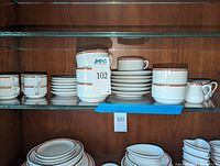 Shelved view showing stacks of cups, saucers and creamer pitchers
