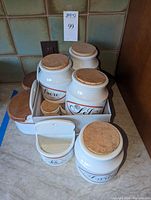 Several white porcelain jars with cork lids on countertop, large and small sizes visible