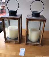 Two Ralph Lauren Home styled wooden lantern holders with glass sides and black metal tops, each containing a white pillar candle, showing slight dust and surface scratching.