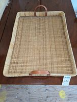 Rectangular wicker tray with leather handles placed on a wooden surface, viewed from above.