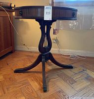 Full view of round lamp table showing harp pedestal base and clawed brass feet.