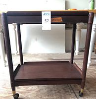 Front view of teak tea trolley showing top and bottom trays, rounded legs and caster wheels