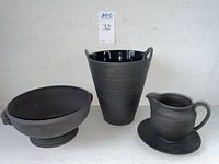 Front view of the three black Wedgwood ceramic pieces: footed bowl, vase, and pitcher with plate visible.