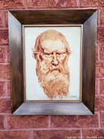 Framed signed painting showing the entire artwork with wooden frame against a brick background.