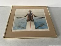 Framed lithograph print of a male sculler rowing on calm water, showing the full framed artwork from an angle.