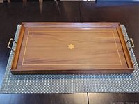 Top view of the rectangular wooden tray showing the inlaid central star design, brass handles, and wood grain.