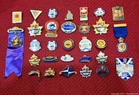 Full view of a collection of 30 vintage pins arranged neatly on a red background, exhibiting various logos, colors, and ribbon attachments.