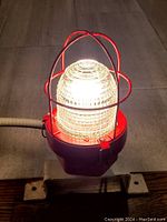 Lamp illuminated showing the protective cage and ribbed glass diffuser glowing when lit.