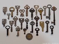 Top view photo showing all 26 vintage small collectible keys arranged in rows with a coin for size scale, displaying variety in shape and design.