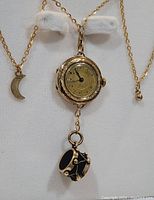 Front view of vintage necklace showing round watch pendant with Roman numerals and hanging black drum charm, crescent moon charm on chain.