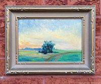 Framed oil painting showing a landscape scene with sky, grassy hills, and a single tree near the center, framed in a decorative silver-tone frame.