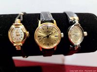 Photo showing three wristwatches on display stand, detail on shapes and straps visible