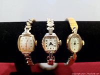 Photo of three vintage women's wristwatches displayed on a black cushion stand showcasing different shapes and metal bands.