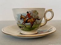 Side view of tea cup showing horse and jockey, gold trimmed handle and rim, with part of matching saucer