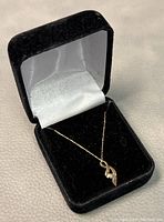 Gold necklace with ribbon style pendant in black velvet jewelry box.