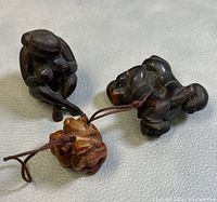 Two netsuke carvings connected by cords showing a double Buddha figure and a triple monkey figure, placed on a light fabric surface