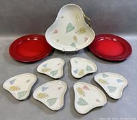 Seven-piece Wunsiedel Bavaria porcelain triangle plate set arranged with two red Le Creuset plates, showing overall lot contents.