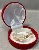 Double-strand hand-knotted white pearl bracelet inside a red velvet box with white satin lining, showing the 14K gold clasp closed and the pearls neatly arranged.