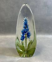 Front view of teardrop crystal paperweight showing blue flower and green leaves