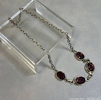 Full view of the necklace laid out showing the five faceted amethyst stones set in sterling silver and the chain with clasp.