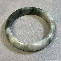 Close-up photo of the round jade bangle placed on a white textured surface, showing green and white marbling.