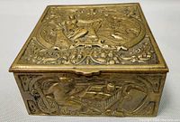 Close-up of top surface of bronze trinket box showing seated female figure with swan and floral-relief border.